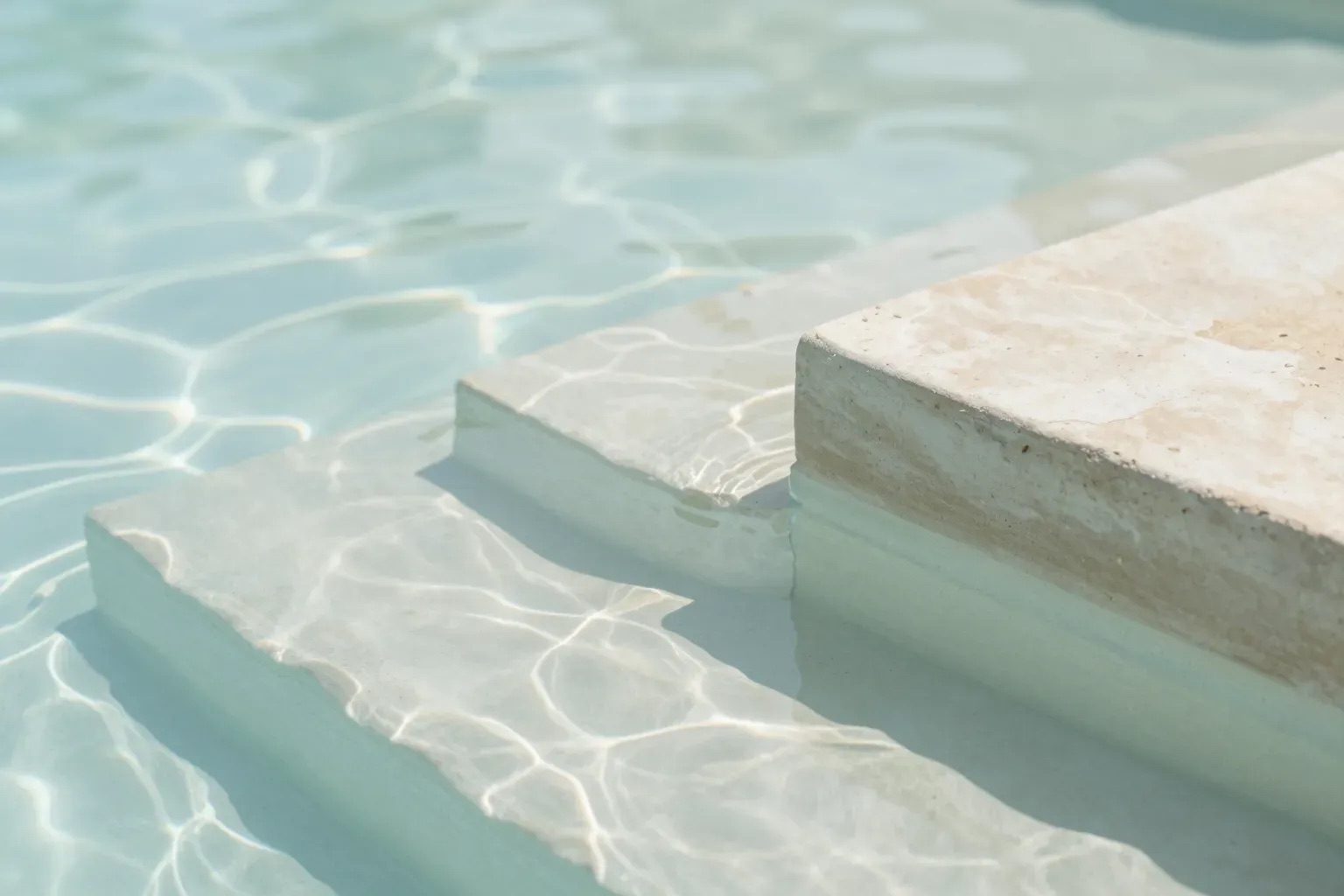 Calm water casting light patterns over pale stone pool steps.